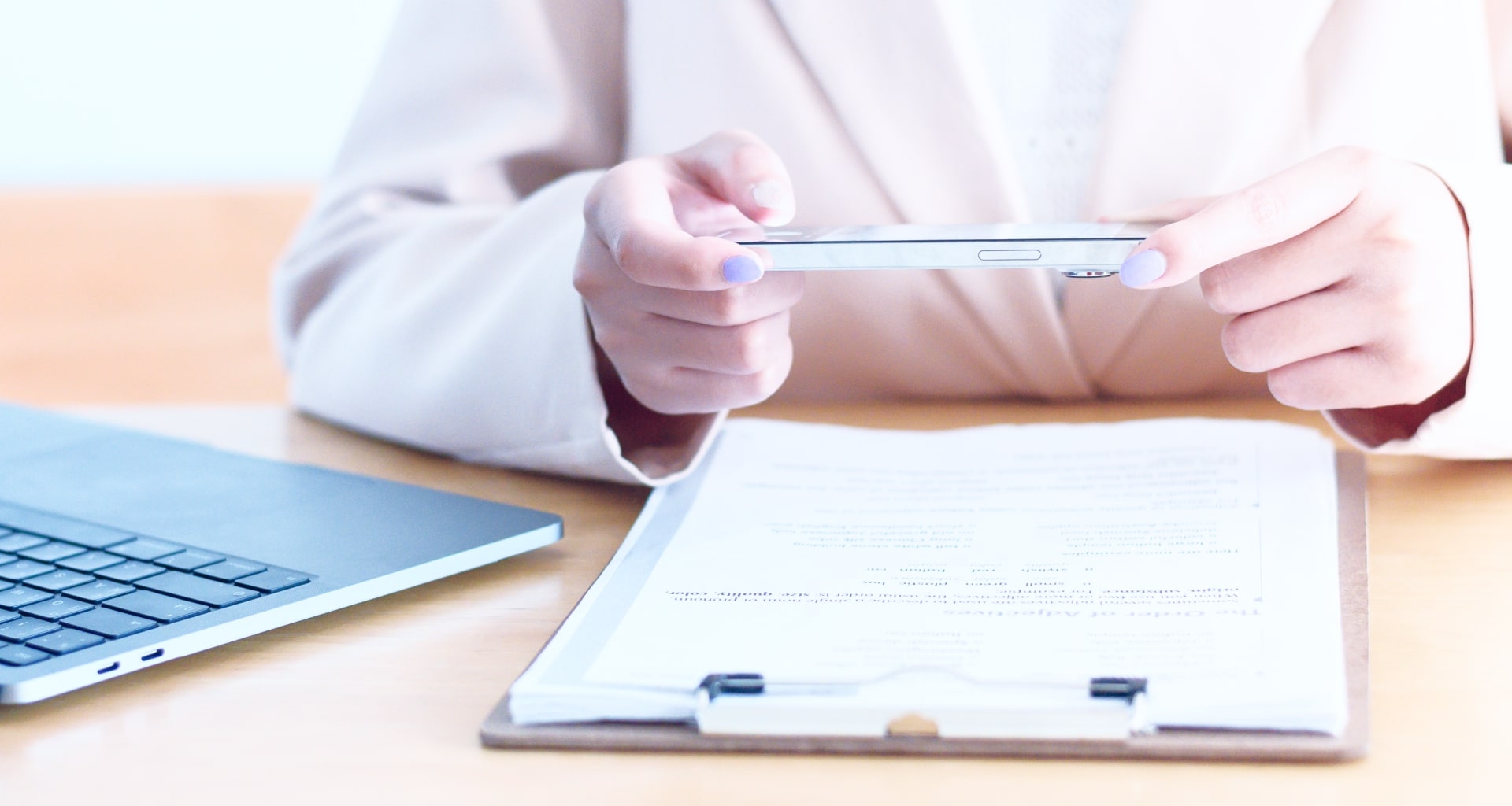 Person using smartphone to scan a physical document on clipboard next to laptop.