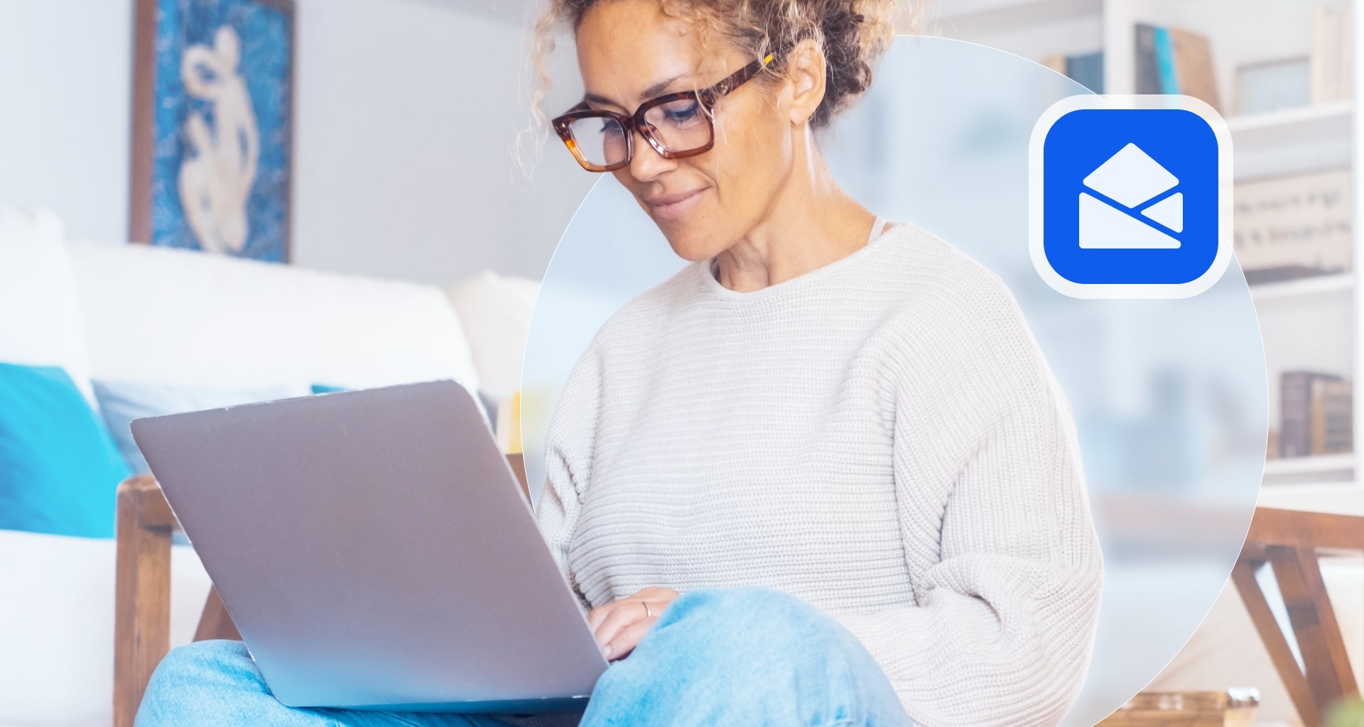 Woman with curly hair wearing glasses working on laptop in home environment with email icon overlay.